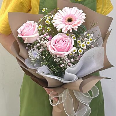small bouquet of pink roses and pink gerbera daisy in brown wrapping